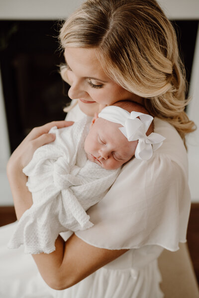 Motherhood photo looking down on mom holding baby against shoulder while wearing white in a studio in Annapolis Maryland.