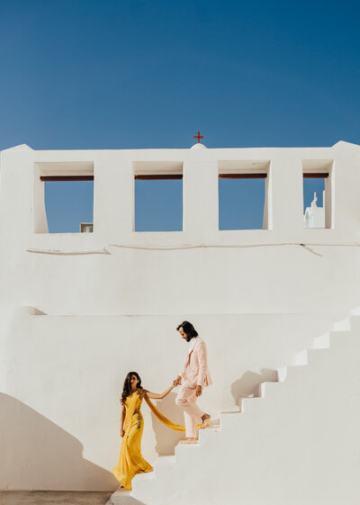 bride and groom holding hands while walking down the steps in Santorini