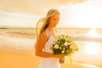 maui bride looks at her bouquet on the beach after eloping in wailea with love and water photography