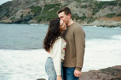 couple in hiking gear laugh other on a rocky shoreline 