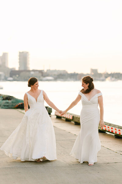 Two brides hold hands as the walk next to the Boston Seaport