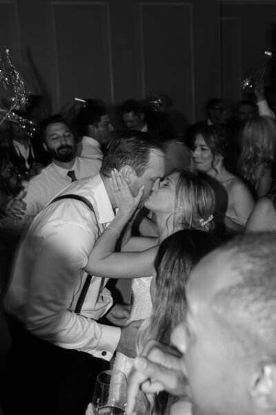 Bride and groom kissing on a packed dance floor during their wedding reception.