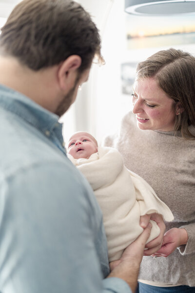 New parents hold their baby wrapped in a white muslin wrap.