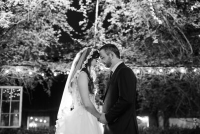 Bride and groom touching foreheads under twinkle lights