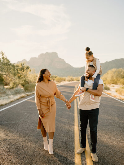 mom and dad with daughter on shoulders walk down arizona road
