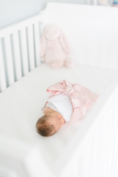 Newborn baby wrapped in a Beaufort Bonnet Co bow swaddle in her white crib