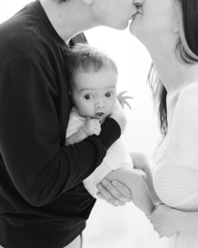 Parents kiss above surprised 3 month old baby