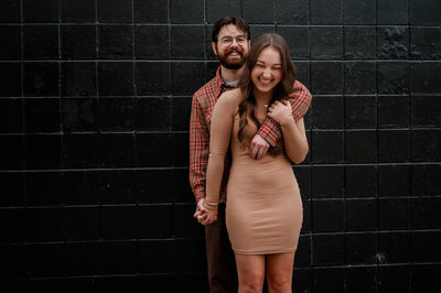A couple poses for the camera standing in an open field during golden hour.