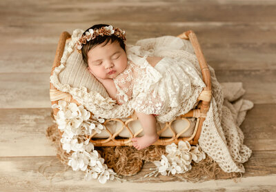 Newborn baby sleeping on cream-toned fabrics with soft, natural studio light.