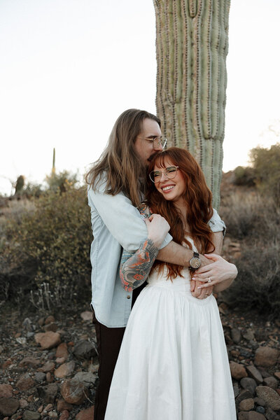 The husband is kissing the top of his  wife's head while she laughs and looks out at the Arizona desert. 
