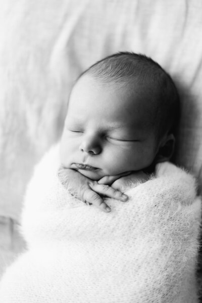 A newborn baby boy swaddled up sleeping in a white fluffy blanket at a newborn photoshoot in Billingshurst