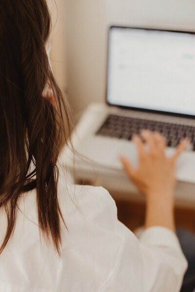 Person wearing ripped jeans and holding a cup of coffee while journaling in a lined notebook, seated in a cozy, casual setting.