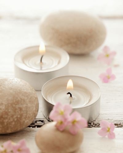 two tea light candles surrounded by rocks and cherry blossoms on a brightly lit background
