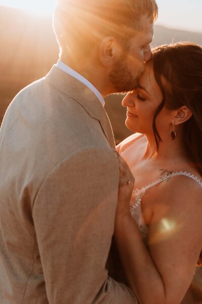 close up of groom kissing brides forehead at sunset