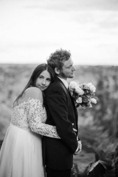 bride hugs grooms back in front of mountain landscape