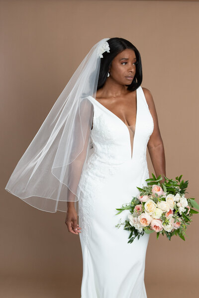 Bride wearing a short serged edge veil with lace headpiece and holding a bouquet