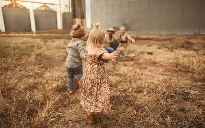 The joy of family moments at Silos McKinney in our captivating photography session. The parents await their kids with open arms as both youngsters sprint towards them, creating a heartwarming scene of love and connection. Dressed in cozy autumn outfits, this family radiates warmth against the scenic backdrop of Silos McKinney
