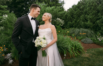 The groom and the bride are holding hands and walking up the stairs, the bride has turned around and is looking at the camera