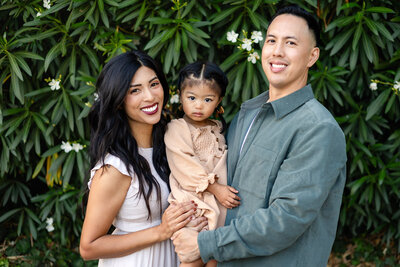 Smiling family with toddler in front of lush greenery by Ellobelle Photography family photographer