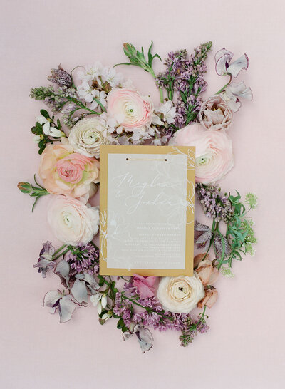 Yellow wedding invitations with a vellum overlay on a bed of flowers, created by Paper Refinery