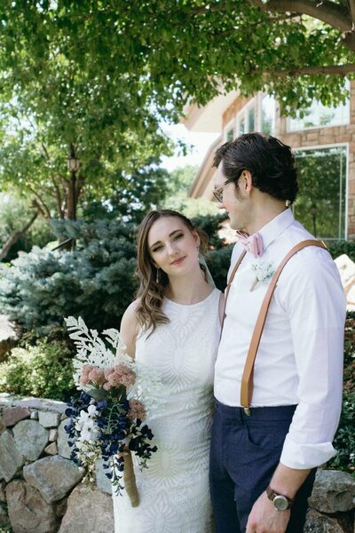 A bride holds her bouquet and looks at the camera while the groom looks at her.