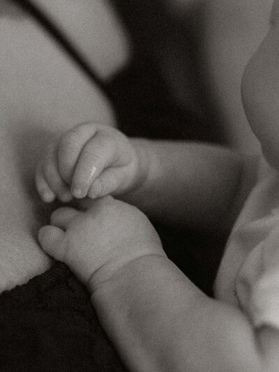 A close-up of baby's little hands while tenderly resting on mom's chest in black and white.
