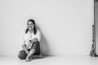 Woman sitting against a wall with legs crossed smiling at camera.