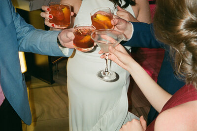 Close up of four peoples hands cheersing their cocktails together