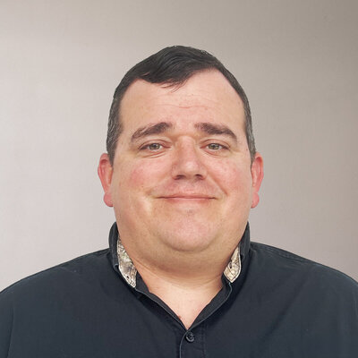 Construction accountant specializing in services for custom home builders, wearing a black collared shirt and smiling confidently.
