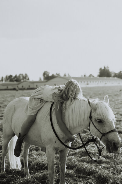 Black and white photo of a little girl sitting on a horse leaning down and hugging the horses neck, taken by a langley photographer