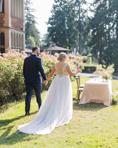 Photo of bride and groom at Thornewood Castle in Seattle holding hands and walking away towards their sweetheart table