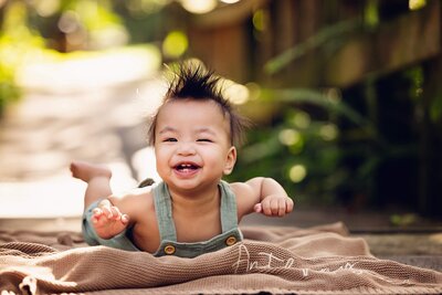 A smiling baby rests on a cozy blanket, capturing a precious moment in a milestone photo session.