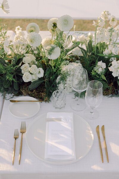 Cream wedding table setting with gold accents and fresh green and white florals