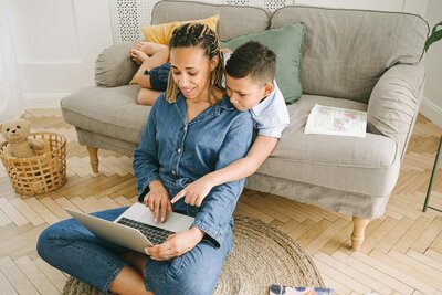 A mom on her laptop with her son next to her. 