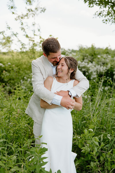 A bride and groom embracing on their wedding day in a field of tall grass and flowers