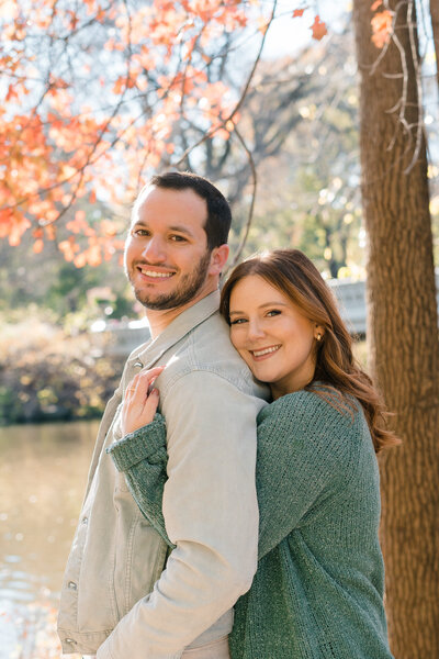 woman hugging man from behind while they are both smiling at camera