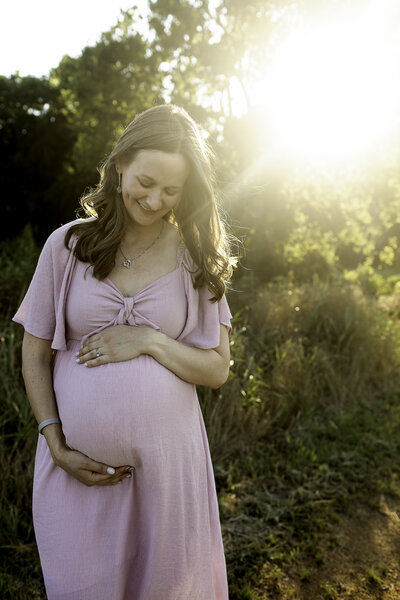 A beautiful maternity photo of the expectant mother wearing a soft pink dress, lovingly hugging her belly with a peaceful smile, captured by Chunky Monkey Photography.