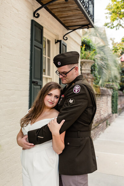 Brown haired girl in white jumpsuit hugging the arm of her groom dressed in a green army suit by Charleston Wedding Photographer, Stephanie Bailey Photography
