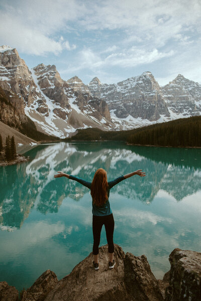 woman standing on rock in front of blue lake with mountains in background