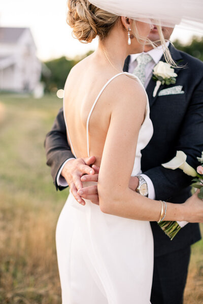 Groom embraces bride in a backless gown at Kent Island Resort
