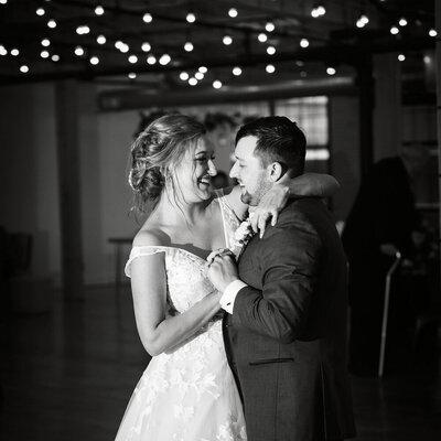 bride and groom share first dance under lights in black and white