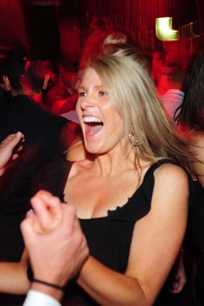 Woman in a black dress laughing and dancing with a crowd in a red-lit Melbourne nightclub or event venue.