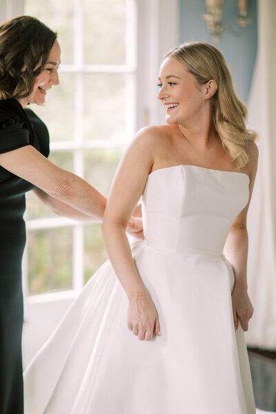 Mother of the bride helps her daughter get dressed in her wedding gown