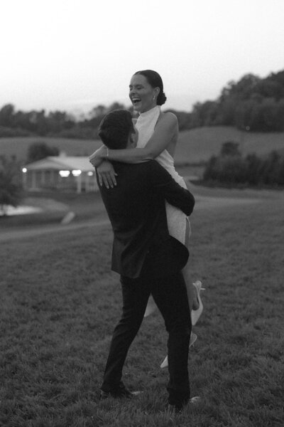 Black and white image of groom spinning bride in the grass at Nashville vineyard wedding