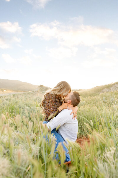 Stunning portrait of a couple kissing as she straddles him on a blanket in an open field.