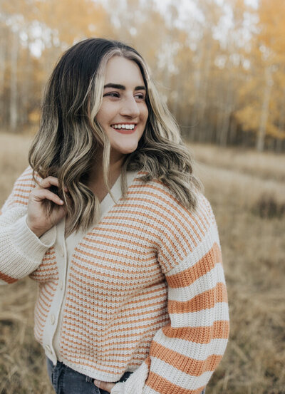 A woman smiles standing in front of fall leaves