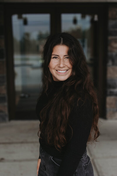 Event planner in cozy winter outfit and grey beanie smiling in snowy Banff forest – Rocky Mountain Wedding Collective