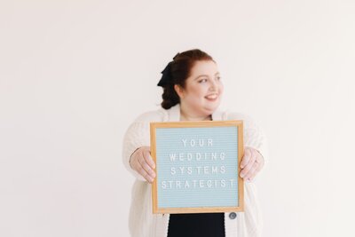 woman holding a sign that says, "your wedding systems strategist"