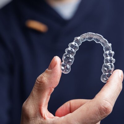 Prosthodontist at Peak Prosthodontics holding a clear aligner for full mouth reconstruction, featuring discreet, custom-made aligners to gently straighten teeth, serving Lethbridge, Alberta and surrounding area.
