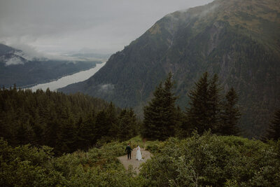 Bride and groom stands overlooking Alaskan fjord.